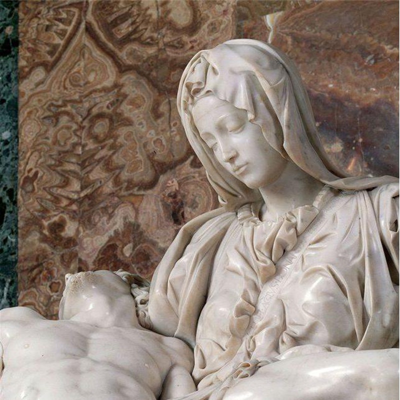 Крупный план лица Девы Марии из скульптуры «Пьета» Микеланджело. Деталь беломраморной статуи с нежными чертами лица и спокойным выражением.